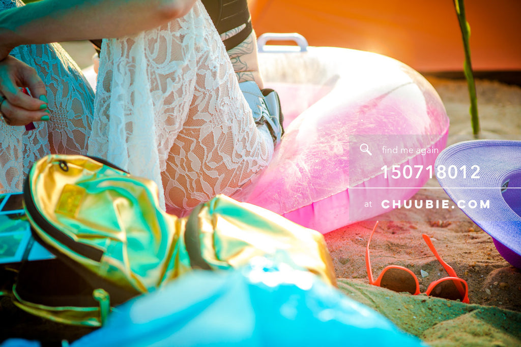 150718012 | 
Lifestyle closeup: Woman in white lace pants sits of colorful pool toys reflecting sunchine on b... | Team Chuubie