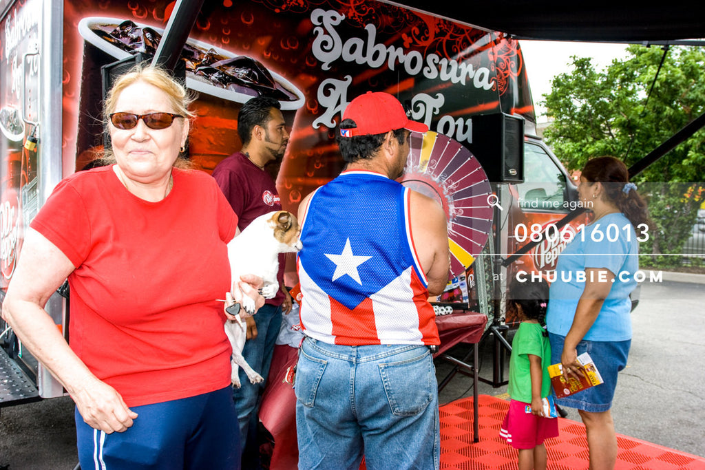 080613013 | 
Local resident woman holds her dog, while man in puerto rican flag tank top spins the wheel.

—D... | Team Chuubie