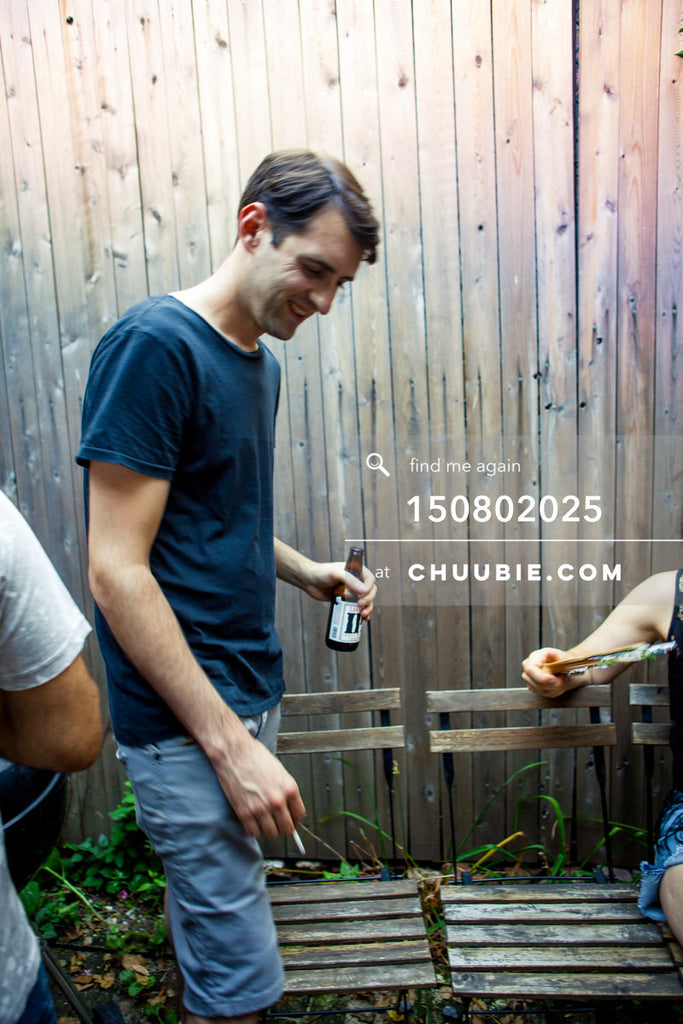 150802025 | Faso smiles with a beer at summer LES backyard BBQ. Wood fence, chairs, greenery.
—Team Fun BBQ h... | Team Chuubie